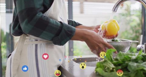 Washing bell pepper at kitchen sink with social media reaction emojis and fresh greens