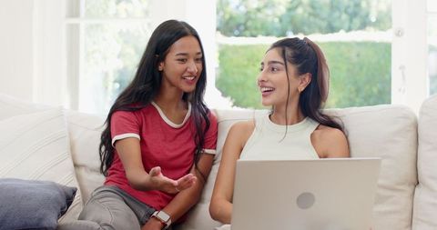 Two Female Friends Sitting on Sofa Collaborating on Laptop