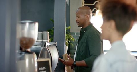 African american man ordering takeout coffee at espresso bar holding to-go bag
