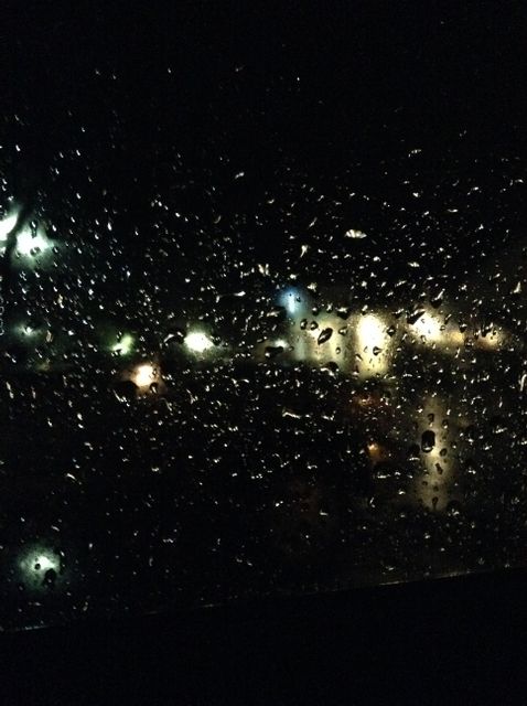 Rain droplets on a window at night showing glimmering lights outside creating an abstract, moody atmosphere. Useful for backgrounds, illustrating mood, depicting weather conditions, or evoking emotions in creative projects.
