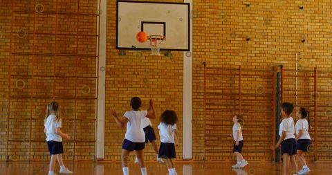 Elementary kids shooting basketball in school gym practicing teamwork during pe class