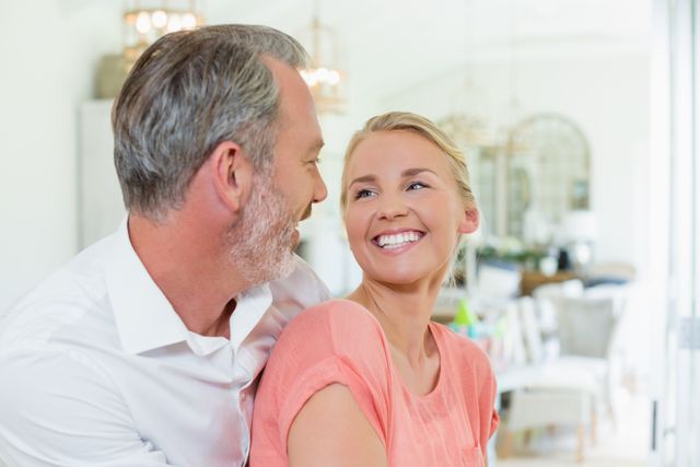 Middle-aged couple embracing and smiling in a modern, well-lit kitchen. Ideal for use in advertisements, blogs, or articles about relationships, home life, and happiness. Perfect for illustrating concepts of love, togetherness, and domestic bliss.