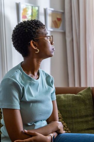 Contemplative african american woman sitting on sofa looking out window in sunlit interior