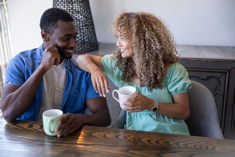Smiling diverse couple enjoying coffee at dining table, casual conversation and cozy comfort