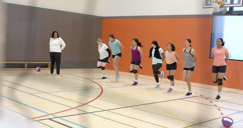 Diverse female volleyball team performing synchronized warmup drills on indoor gym court