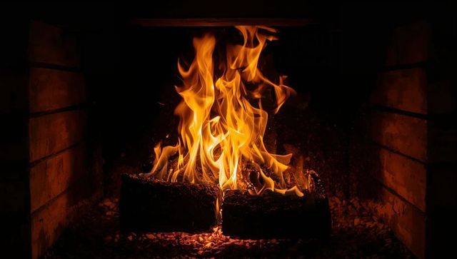 Cozy fireplace flames dancing over burning logs in brick hearth with glowing embers