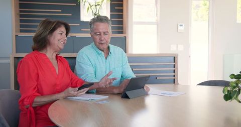 Senior Couple Using Smartphone and Tablet at Home Discussing Digital Technology