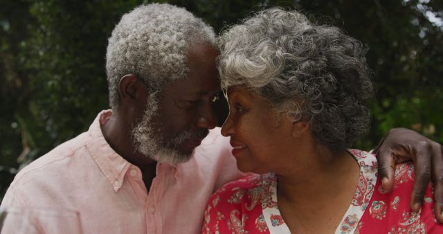 Senior biracial couple shares a tender moment outdoors. Their affectionate gaze reflects a deep and enduring connection.