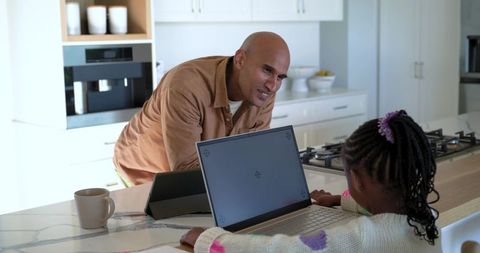 Father mentoring african american daughter using laptop and tablet at modern kitchen island