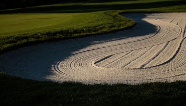 Sunlit raked bunker with sweeping curved lines and shadow on golf green