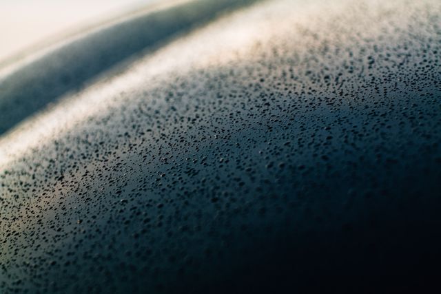 This image captures an abstract close-up of dew drops on a smooth surface, taken in the early morning light. The natural texture of the water droplets adds a unique visual appeal. Ideal for use in nature-themed projects, backgrounds, design inspiration, or moisture-related concepts.