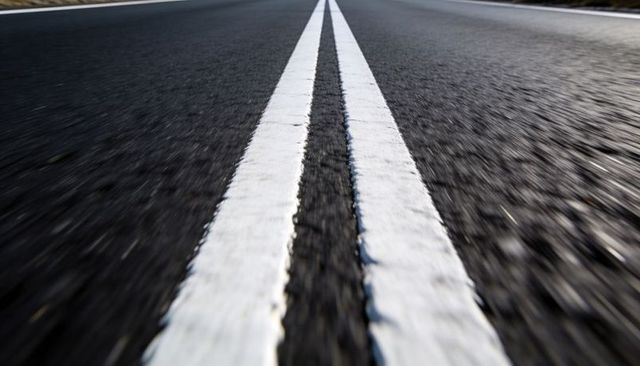 Double solid white center lines leading into distance on textured asphalt road