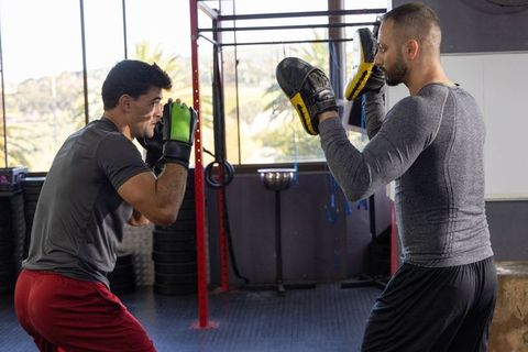 Trainer holding focus pads while trainee sparring in gym sunlit studio