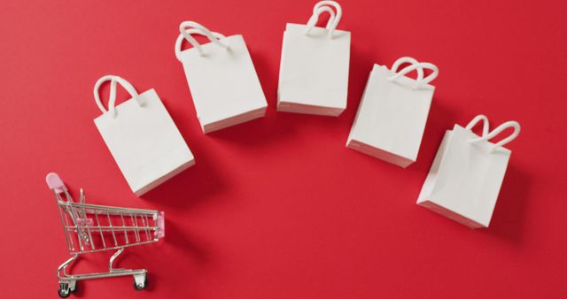 Five white gift bags and shopping trolley on red background with copy space. Luxury treat, present, shopping, sale and retail concept digitally generated image.