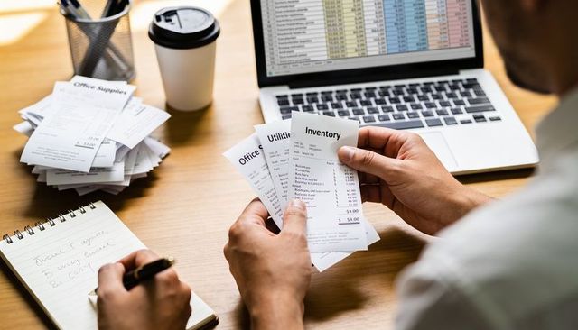 Sorting receipts and reconciling expenses at desk with laptop and notepad for budgeting