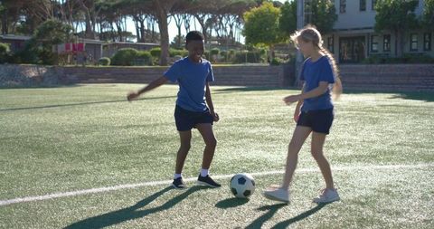 Diverse teens playing soccer on sunny artificial turf, practicing teamwork and passing drills
