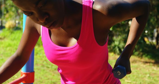 Woman lifting dumbbells while working out outdoors, focused on her strength training. Ideal for use in articles about fitness routines, outdoor exercise, healthy living, and workout motivation.