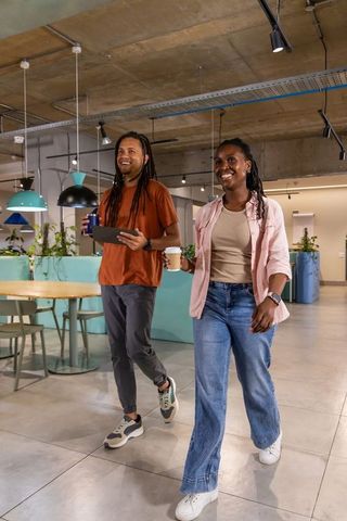 Walking and smiling african american coworkers holding coffee and tablet in modern office