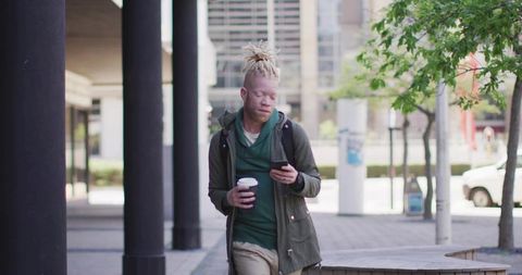 Urban commuter walking and glancing at smartphone holding takeaway coffee in city plaza