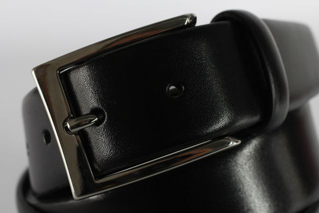 Close-up focusing on a black leather belt with a metallic buckle, highlighting its shiny surface and classic design. Ideal for fashion websites, accessories shops, men's wear catalogs, and lifestyle blogs about wardrobe essentials.