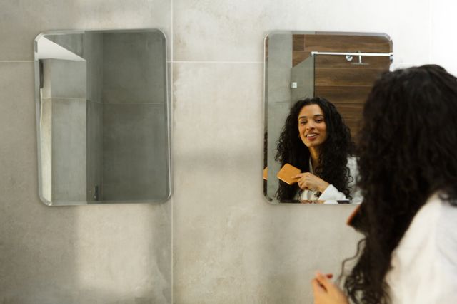 Biracial woman standing in bathroom brushing her hair and smiling. enjoying quality time at home in self isolation during coronavirus covid 19 pandemic.