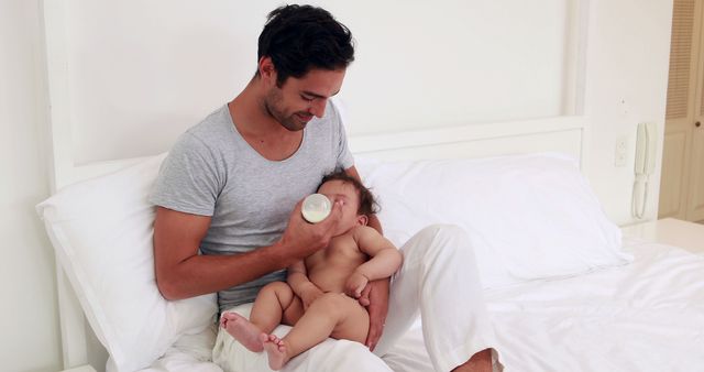 Handsome father feeding his baby on the bed