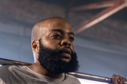 Sweating african american man lifting barbell on shoulders in industrial gym, intense focus