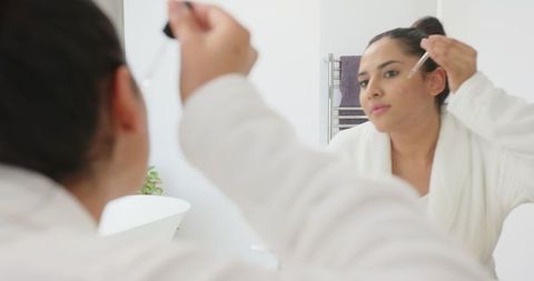 Woman in Bathrobe Applying Serum in Minimalist Bathroom