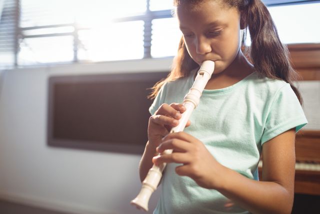 Young girl playing flute in music school classroom. Ideal for content about music education, children's hobbies, classroom activities, and developing musical talent.
