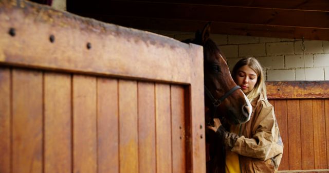 Young woman showing care and affection for her horse in a stable or barn. Ideal for content related to horse care, equestrian activities, and animal companionship. Great for ads and websites promoting horse-riding clubs, agricultural news, or pet care products.