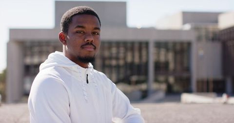 Confident African American man standing arms folded wearing white hoodie on urban plaza