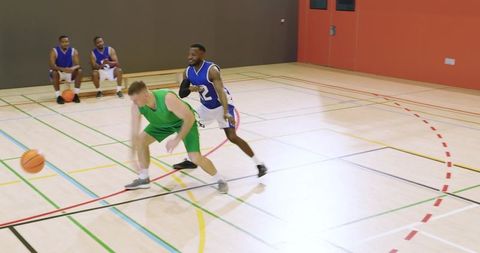 Basketball players competing for loose ball on indoor court during intense game