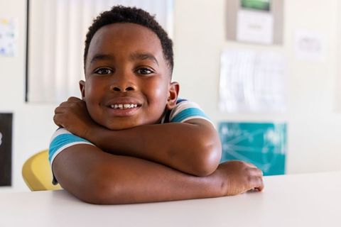 African american boy smiling and leaning on desk in bright classroom portrait