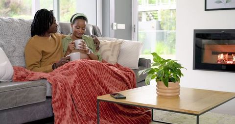 African American couple cuddling on sofa sipping coffee by fireplace in cozy living room
