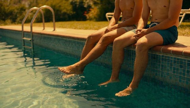 Two young men sitting on pool edge kicking and splashing water summer backyard relaxation