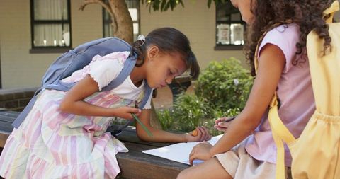 African american schoolgirls studying together on school bench outdoors with backpacks