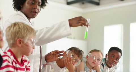 African-american teacher holding green test tube guiding young students during science lab