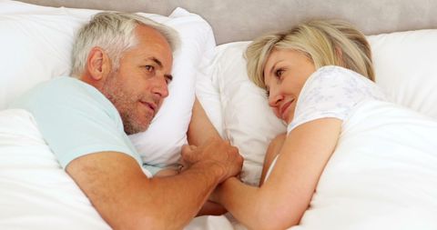 Senior Couple Relaxing in Bed and Holding Hands Smiling