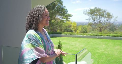Middle-aged woman enjoying balcony view wearing colorful shawl overlooking backyard lawn