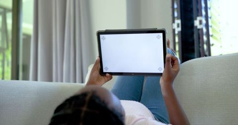 Black teen reclining on sofa holding tablet with blank screen