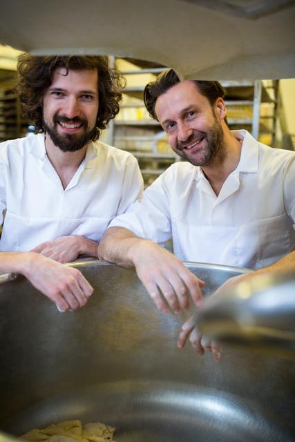 Portrait of two smiling bakers standing near dough machine