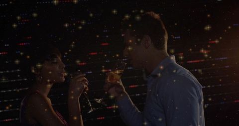 Romantic couple toasting amber cocktails amid sparkling nightlife lights