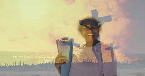 Smiling woman holding yoga mat on coastal shore with cross silhouettes double exposure