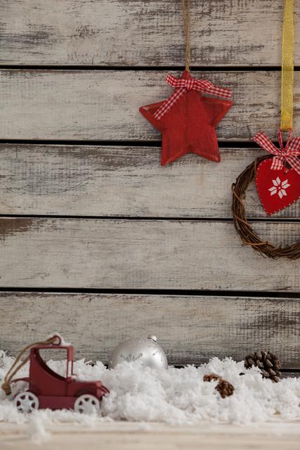 Rustic Christmas decorations featuring a hanging wreath and star against a wooden background. Snow and pinecones add a festive touch. Ideal for holiday cards, seasonal advertisements, and festive blog posts.