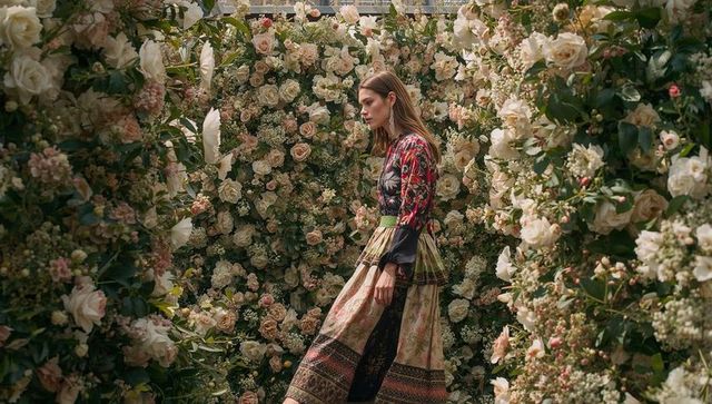 Model walking through rose tunnel wearing patterned maxi dress with green sash editorial