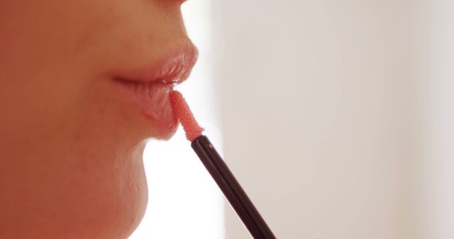 Close-up view of a woman applying lip gloss with an applicator brush. This image can be used in beauty tutorials, cosmetic product advertisements, blogs, or social media posts related to makeup and personal care.