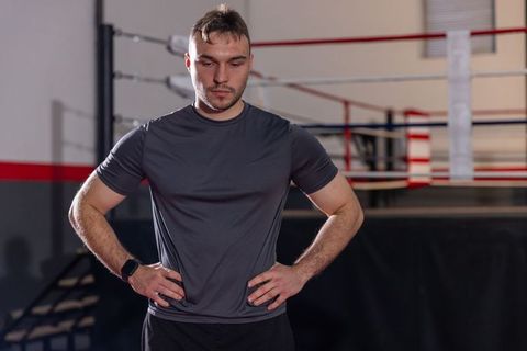 Focused male athlete standing in boxing ring wearing smartwatch and dark training shorts