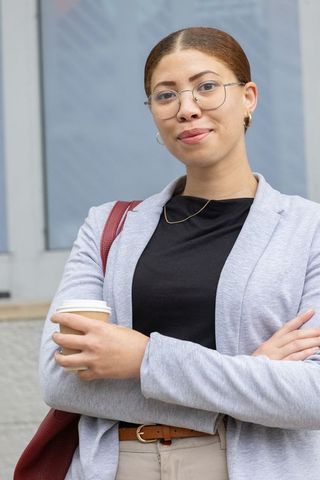 Confident african american businesswoman holding coffee, wearing blazer in urban district