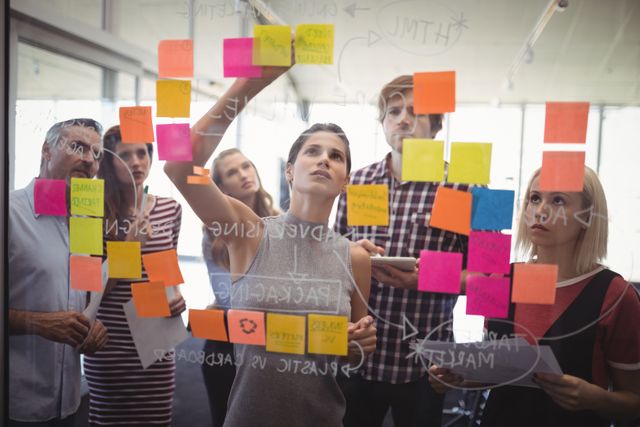 Business team collaboratively planning and brainstorming with sticky notes in a modern office environment. Ideal for depicting teamwork, project management, and collaborative workspaces in business-related content, training materials, and corporate presentations.