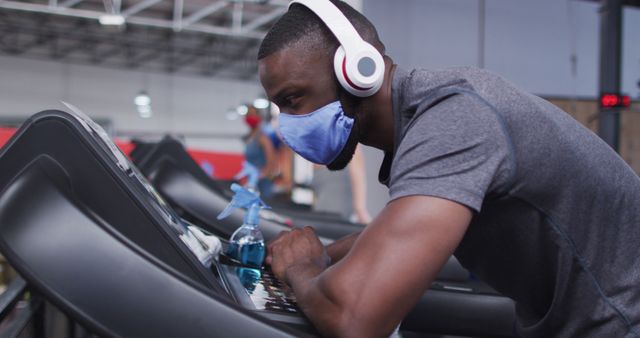 Tired man african american wearing face mask and headphones taking a break while running on treadmill in the gym. social distancing quarantine lockdown during coronavirus pandemic